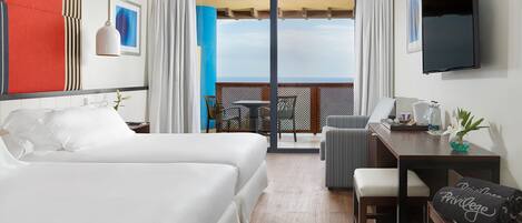 Habitación de hotel con dos camas, un escritorio, una silla, un televisor y un balcón con vistas.