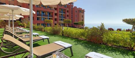 A hotel patio with outdoor seating, a pool, and a view of the sea.