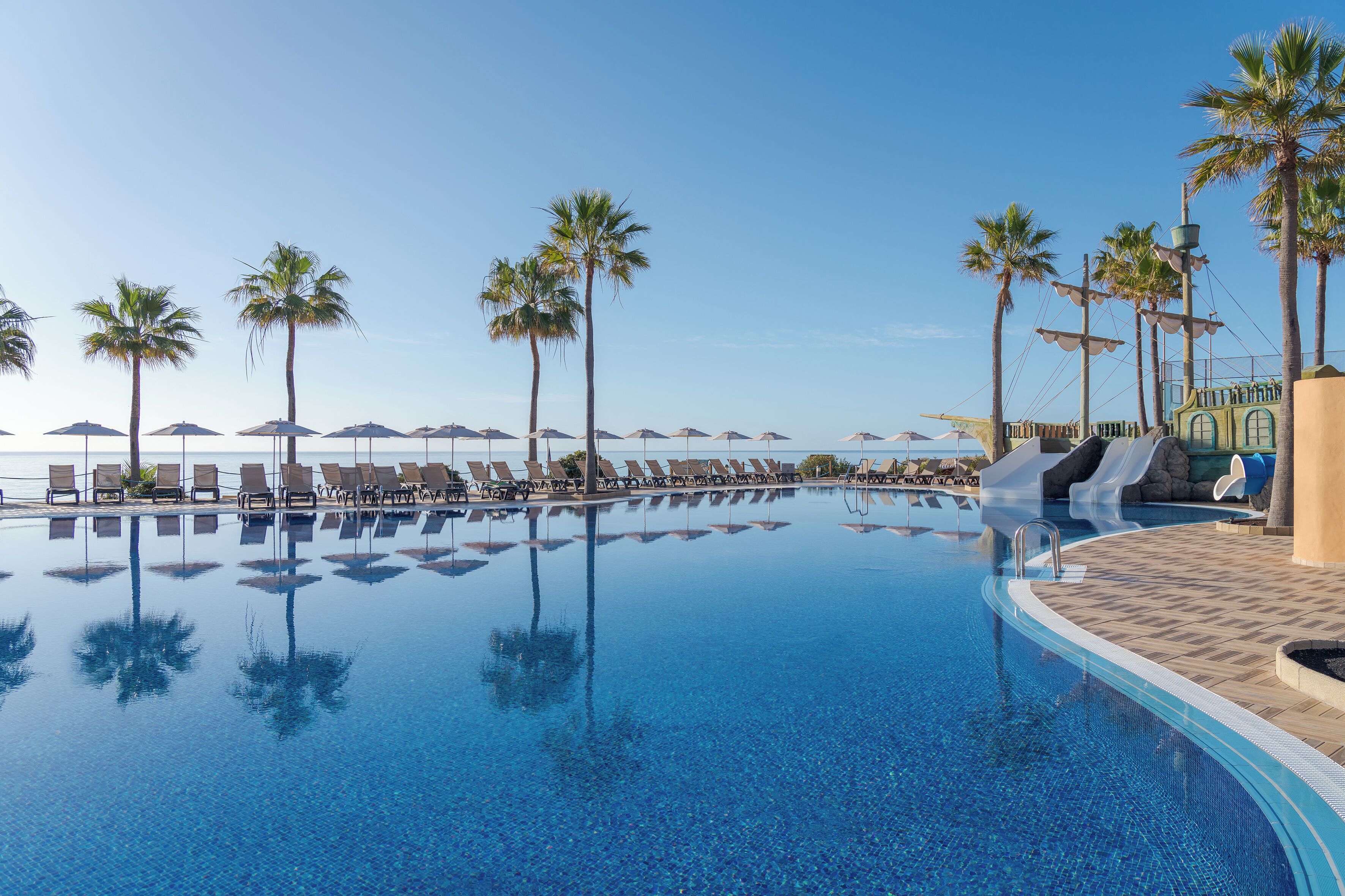 A clear pool with lounge chairs and palm trees.