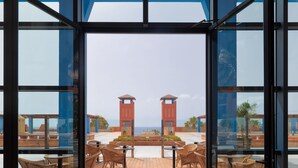 A modern indoor seating area with a view of a pool and palm trees. - H10 Tindaya (Pajara)