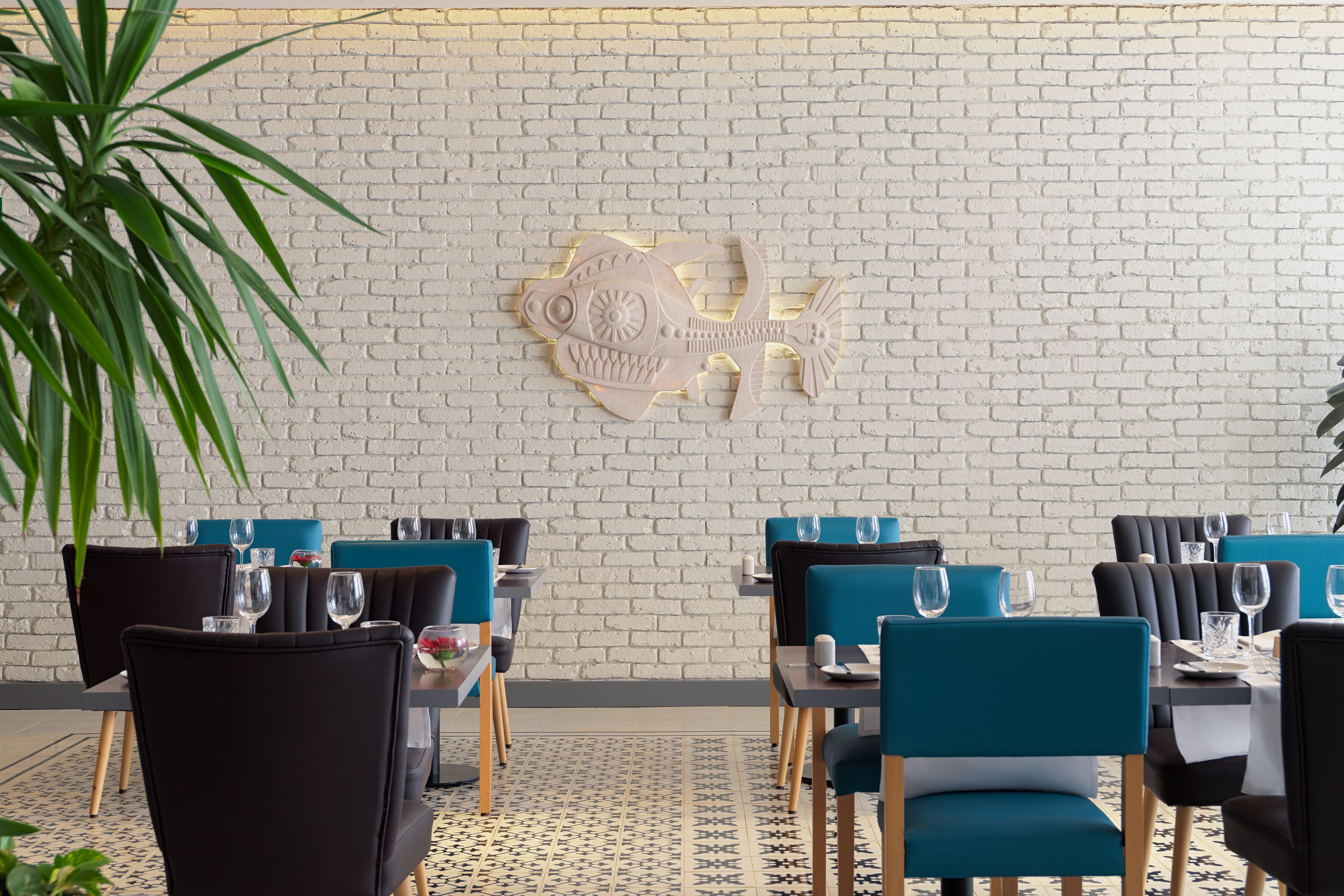 A restaurant with a brick wall and a fish sculpture. Tables are set with chairs and wine glasses.
