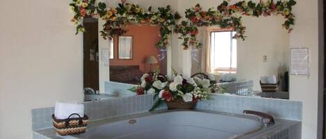 A bathroom with a large bathtub, a mirror, and floral decorations.