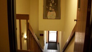 Un pasillo con una escalera de madera, una obra de arte floral enmarcada en la pared y una puerta al final.