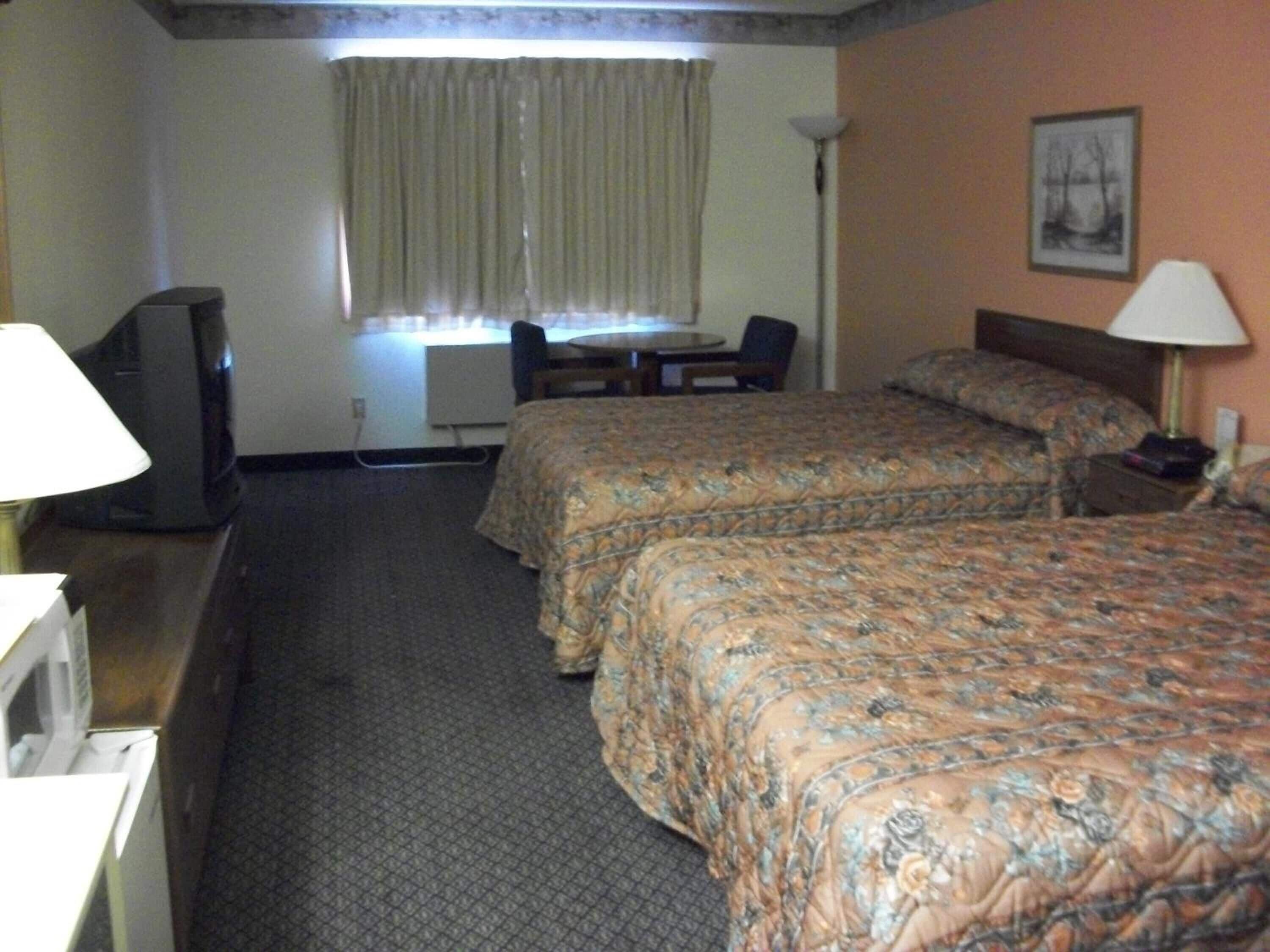 A hotel room with two beds, a desk, a chair, a television, and a lamp.