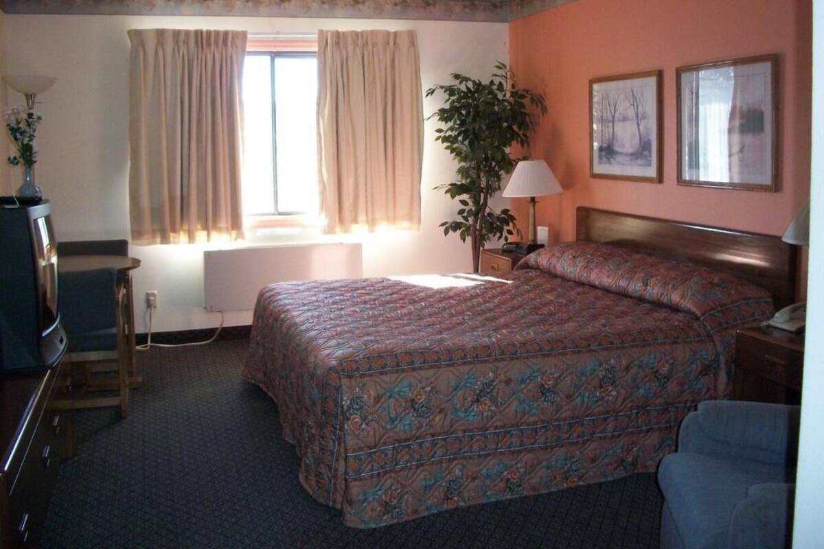 Habitación de hotel con una cama grande, un escritorio, una silla, una lámpara y una ventana con cortinas.