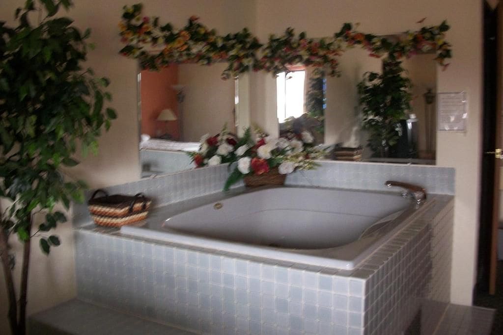 Un baño con una bañera grande, un espejo y un arreglo floral sobre el espejo.