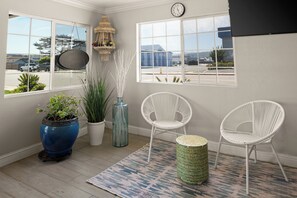 A room with two white wicker chairs, a blue vase with a plant, a woven basket, and a patterned rug.