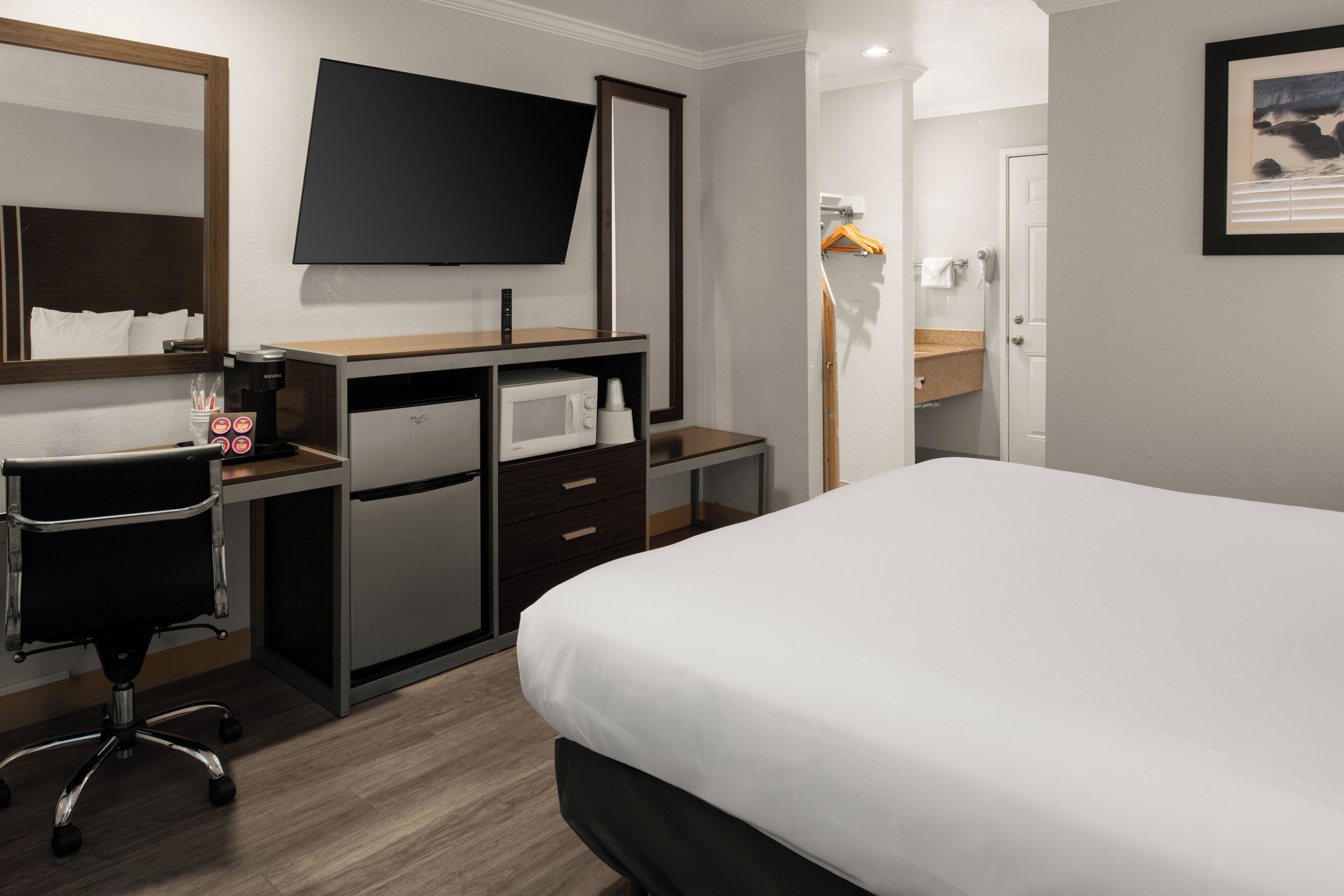A hotel room with a bed, a desk with a computer, a microwave, a TV, and a mirror.