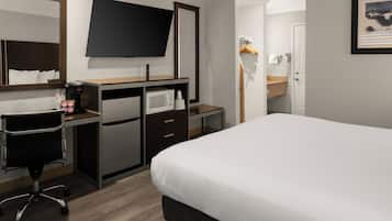 A hotel room with a bed, a desk with a computer, a microwave, a TV, and a mirror.