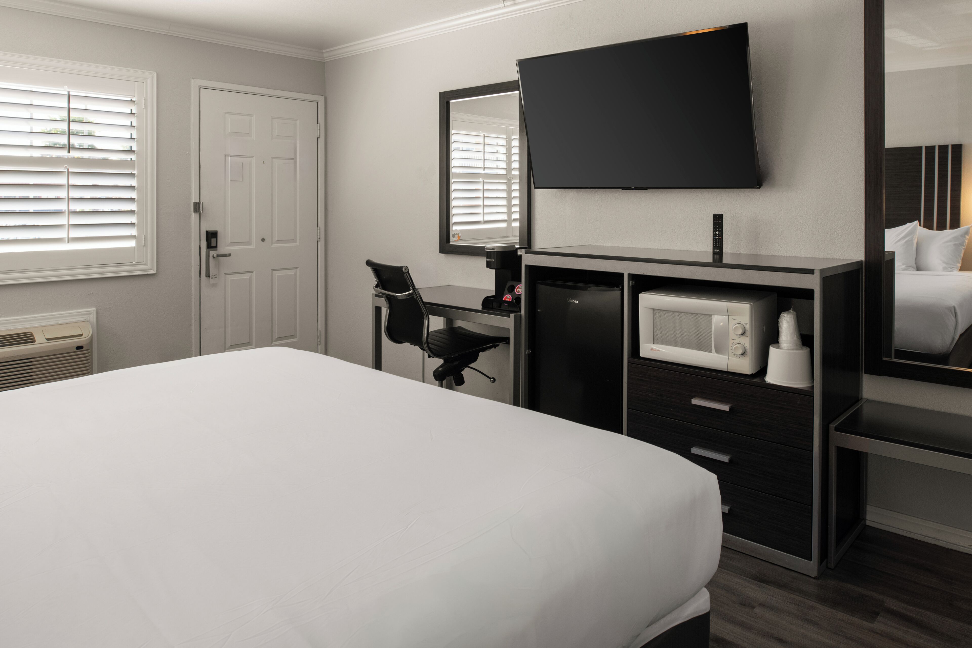 A hotel room with a bed, a desk with a chair, a television, a microwave, and a large mirror.