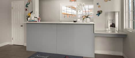 A hotel reception area with a white counter, a window with a view of buildings, decorative fish and starfish on the wall, and a doormat with a castle design.