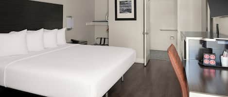 A hotel room with a large bed, a desk with a chair, a small table with a coffee machine, and a framed picture on the wall.