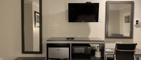 Habitación de hotel compacta con kitchenette, un televisor de pantalla plana, un espejo grande y una silla de oficina moderna.