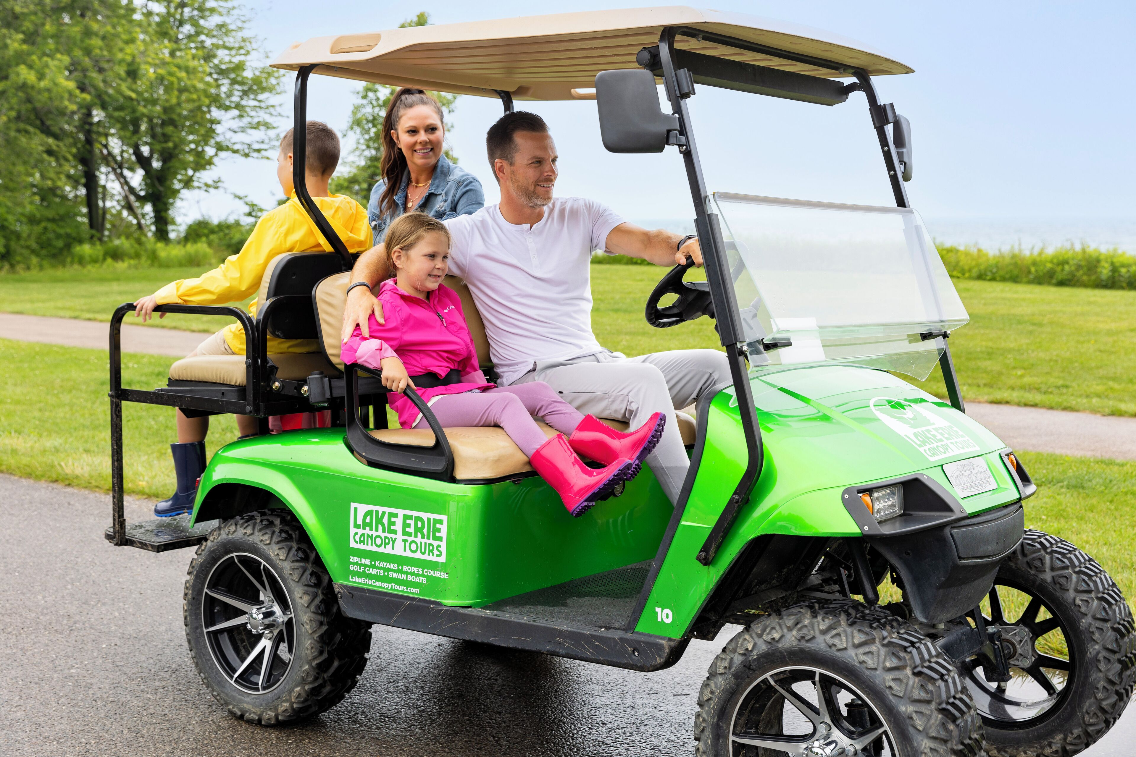 A green golf cart with a canopy, labeled "Lake Erie Golf Tours," on a paved path with grass on the sides.