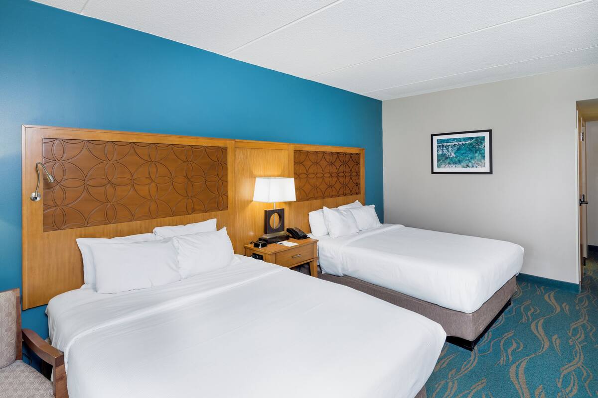 A hotel room with two beds, a wooden headboard, a nightstand with a lamp, and a framed picture on the wall.