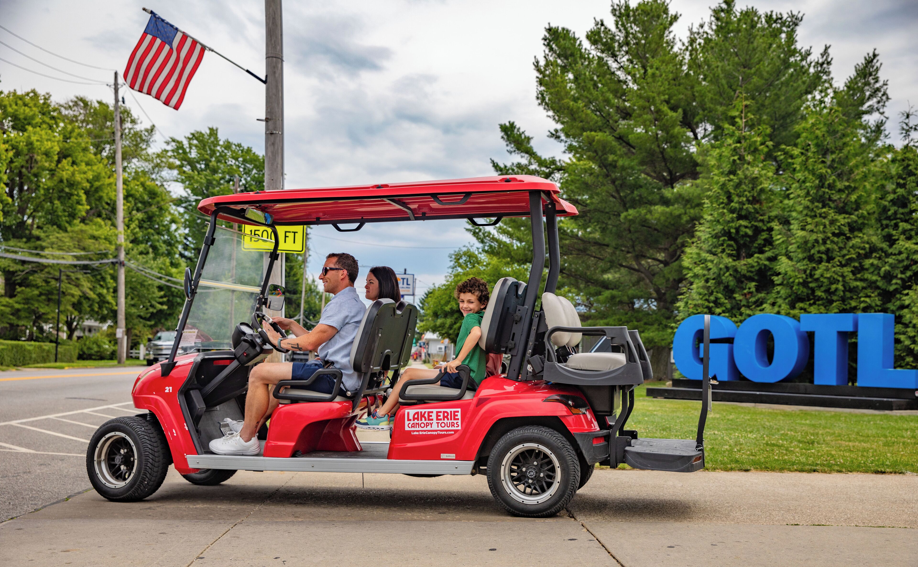 A red golf cart with the text "Lake Erie Canopy Tours" on the side, parked on a street with a "1500 FT" sign in the background.