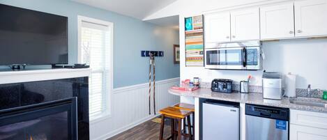 A modern kitchen with white cabinets, a built-in microwave, a dishwasher, and a fireplace.