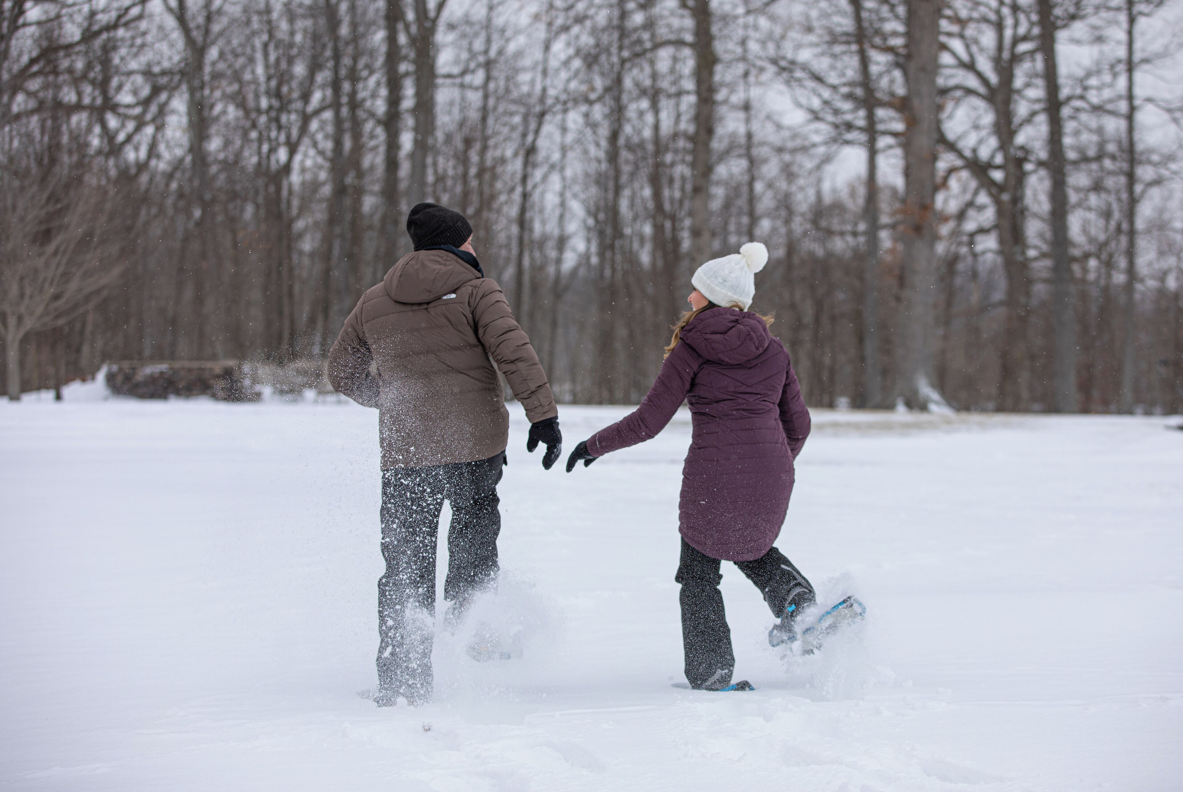 Two people walking in the snow, holding hands.