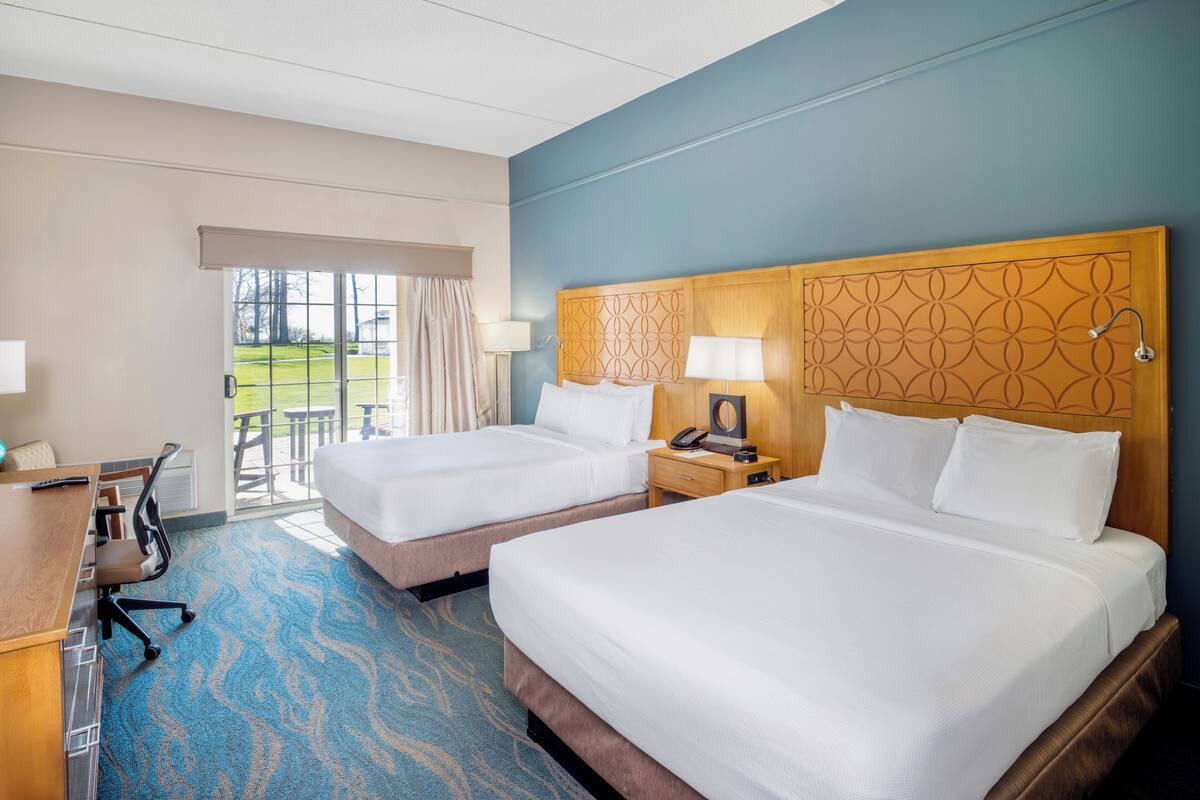 A hotel room with two beds, a desk with a chair, a telephone, and a lamp.