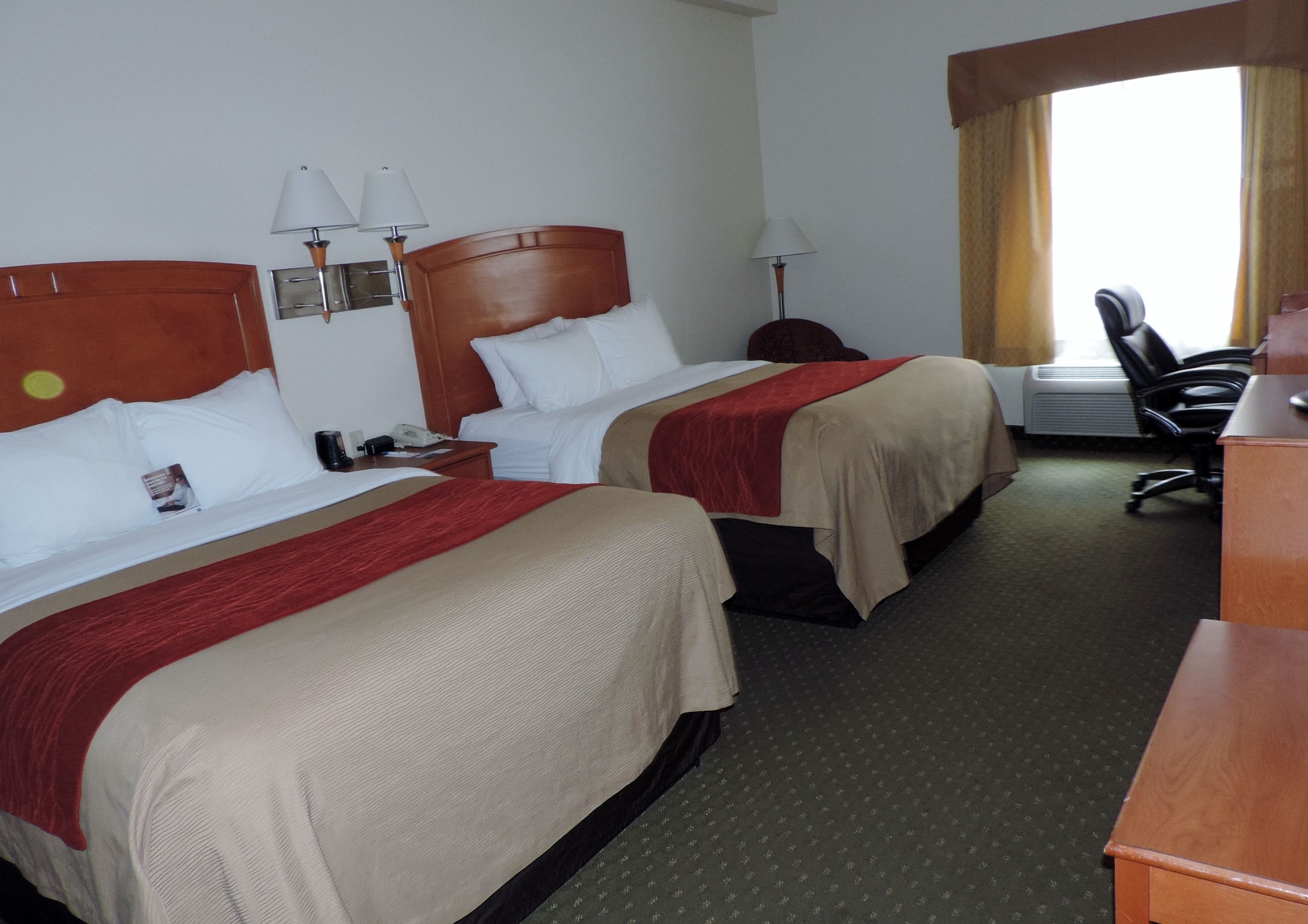 Habitació d'hotel amb dos llits, una taula, una cadira i una finestra amb cortines.