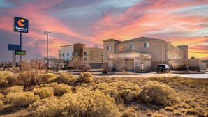 Un hotel Comfort Inn & Suites con un paisaje desértico al frente y un cielo al atardecer.