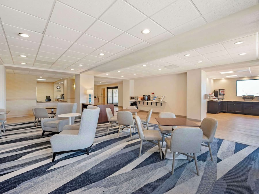 A spacious lobby with a striped carpet, multiple seating areas, a reception desk, and a kitchenette in the background.
