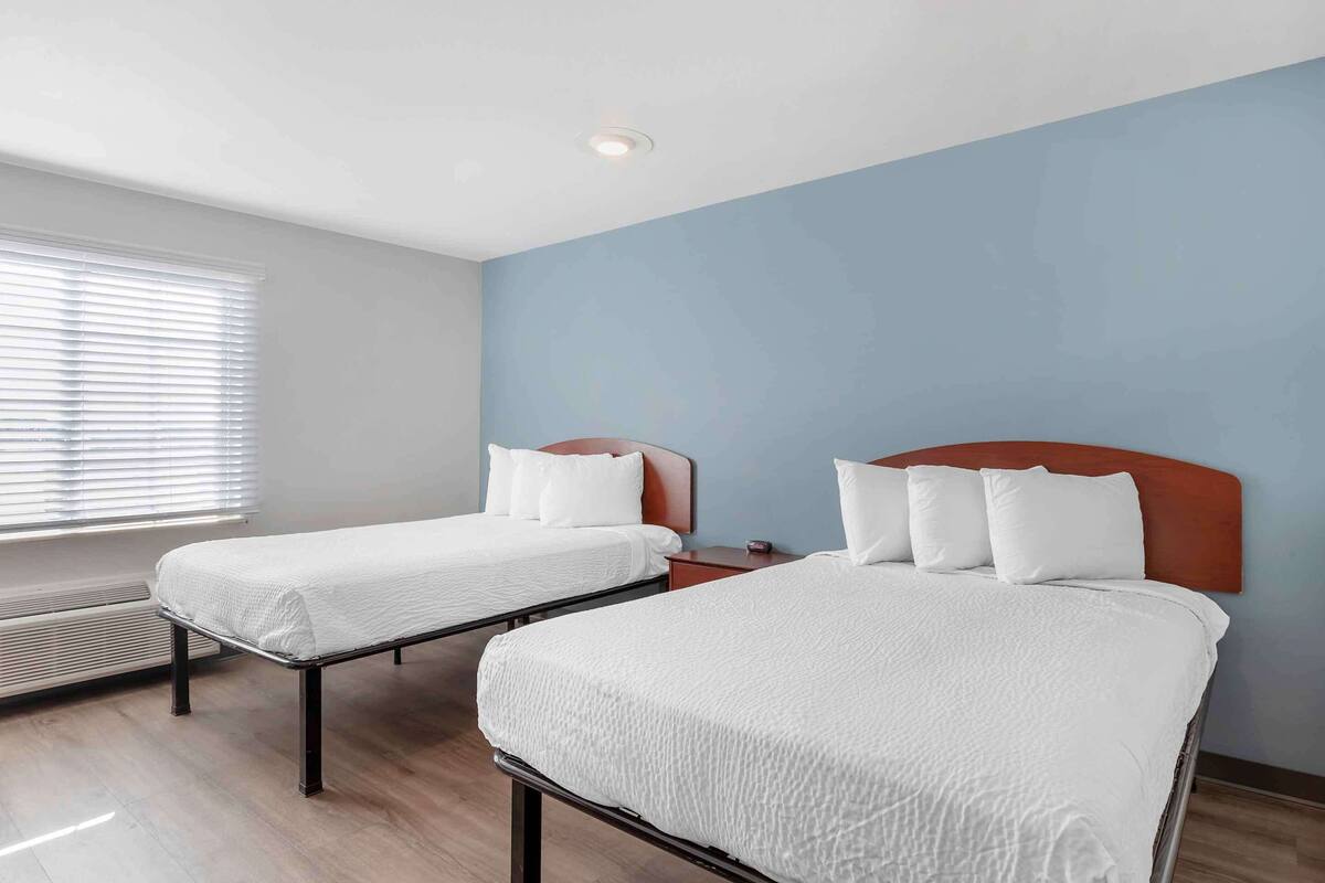 Quarto de hotel com duas camas, uma janela com persianas e um aquecedor de parede.