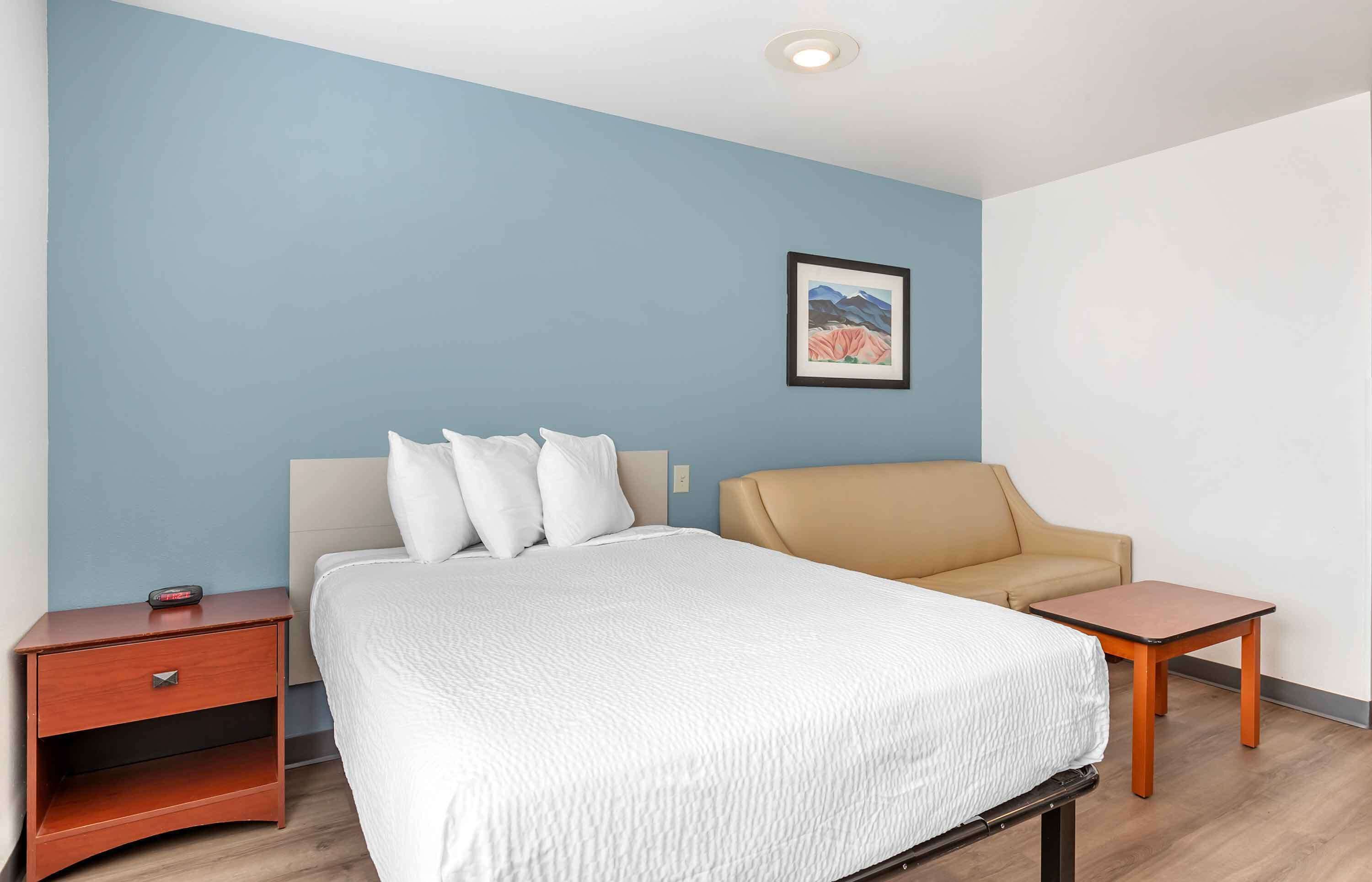 A hotel room with a bed, a chair, a nightstand, and a small table.