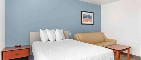 A hotel room with a bed, a chair, a nightstand, and a small table.