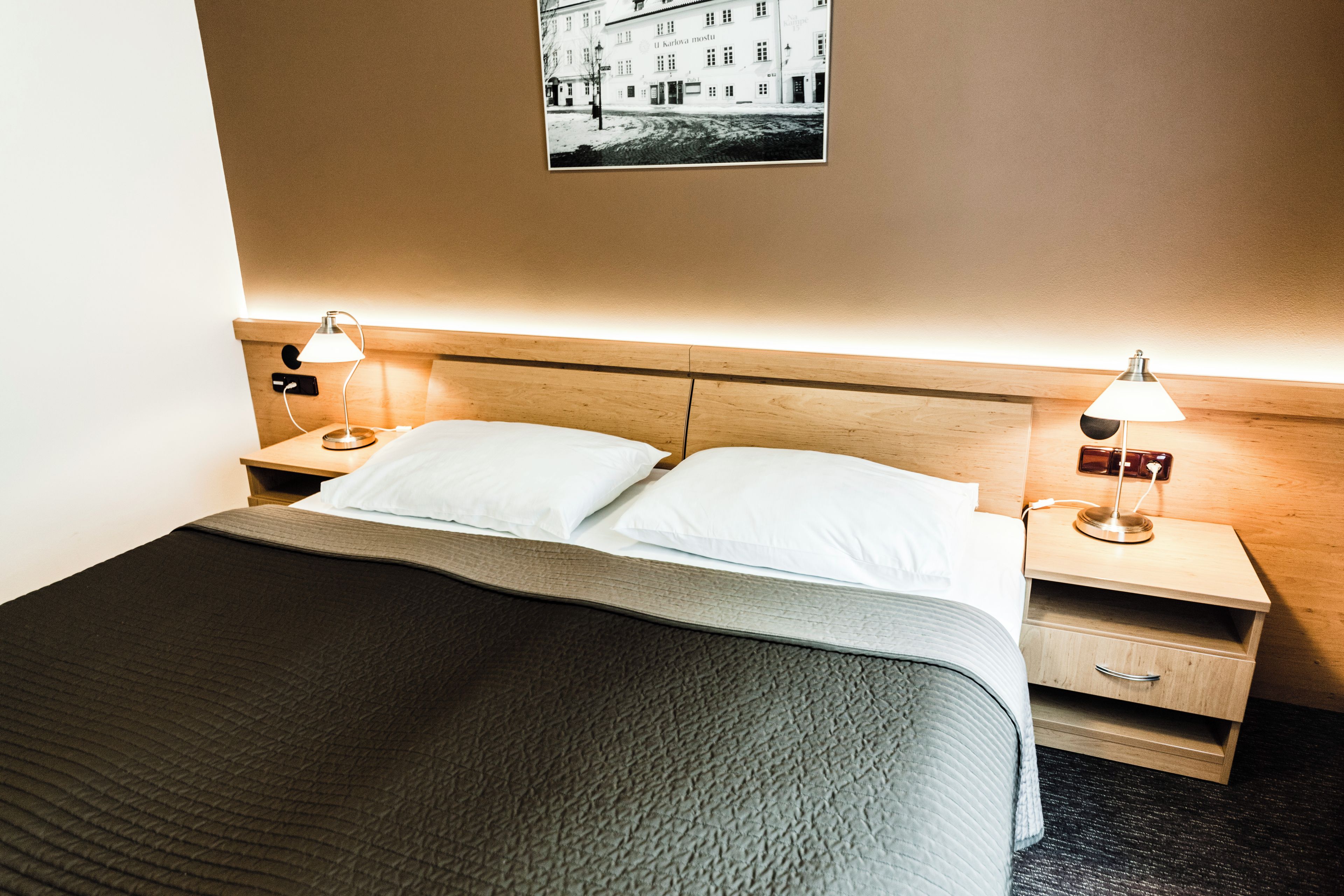 A hotel room with a bed, two bedside tables with lamps, a wall-mounted picture, and a wooden headboard.