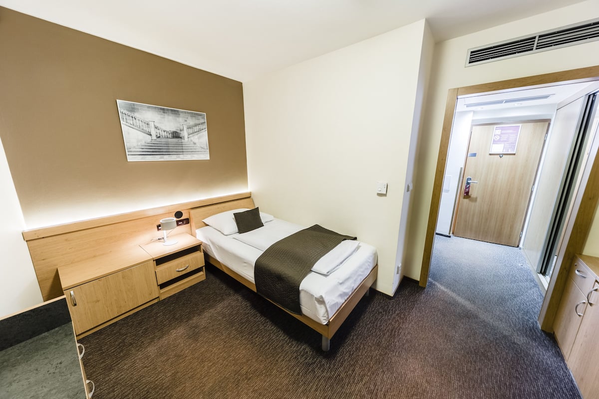 A hotel room with a bed, a desk, a chair, a wall-mounted picture, and a door.
