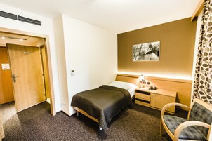 Quarto de hotel com cama, mesa de cabeceira, cadeira e um quadro na parede.