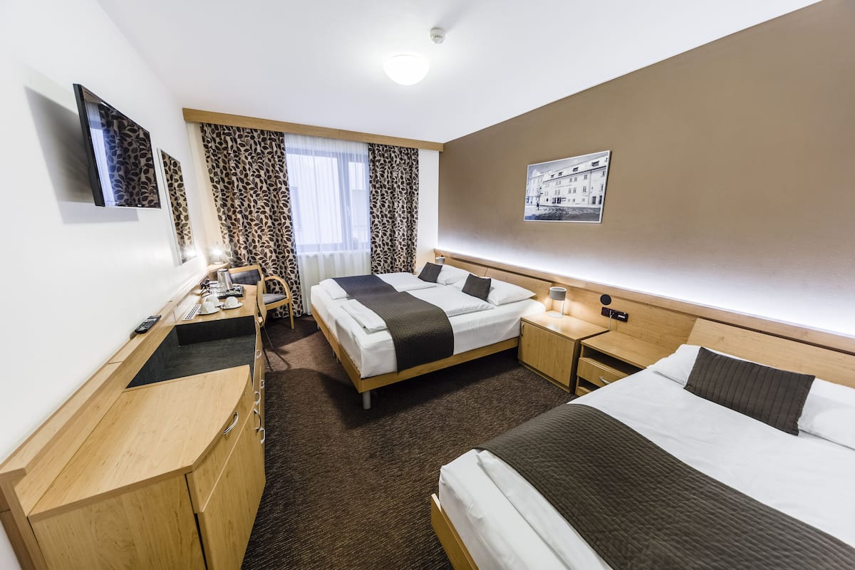 A hotel room with a bed, a desk, a chair, a wardrobe, a bedside table, and a window with curtains.
