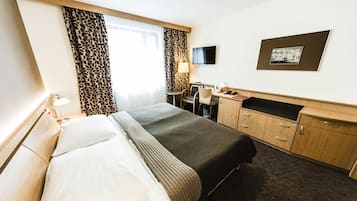 A hotel room with a bed, desk, chair, and a television on the wall.