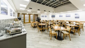 A spacious dining area with multiple tables and chairs, a buffet counter, and a high ceiling with skylights.