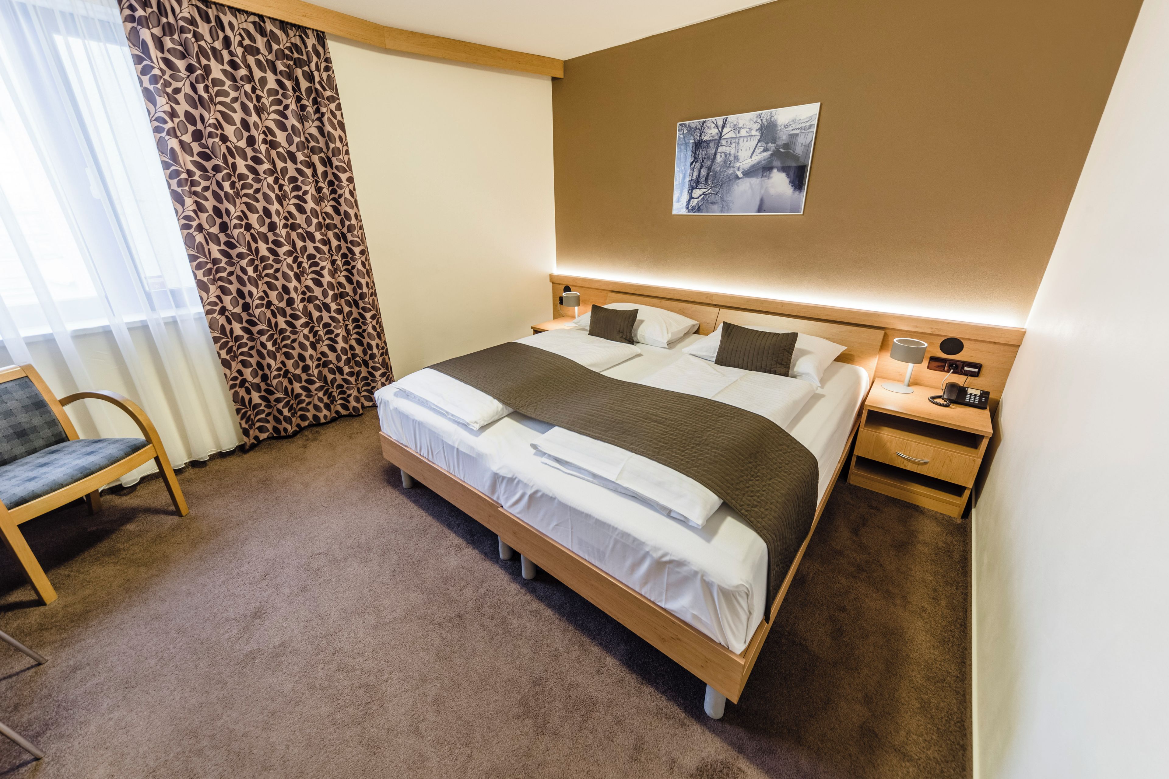 Une chambre d’hôtel avec un grand lit, une table de chevet avec une lampe, une chaise et un tableau au mur.