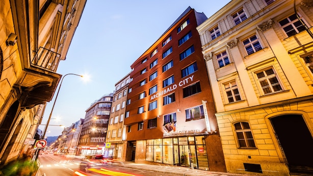 A multi-story hotel with a classic facade, a prominent sign reading "ARCHIBALD CITY HOTEL," and a street view with light trails indicating traffic.