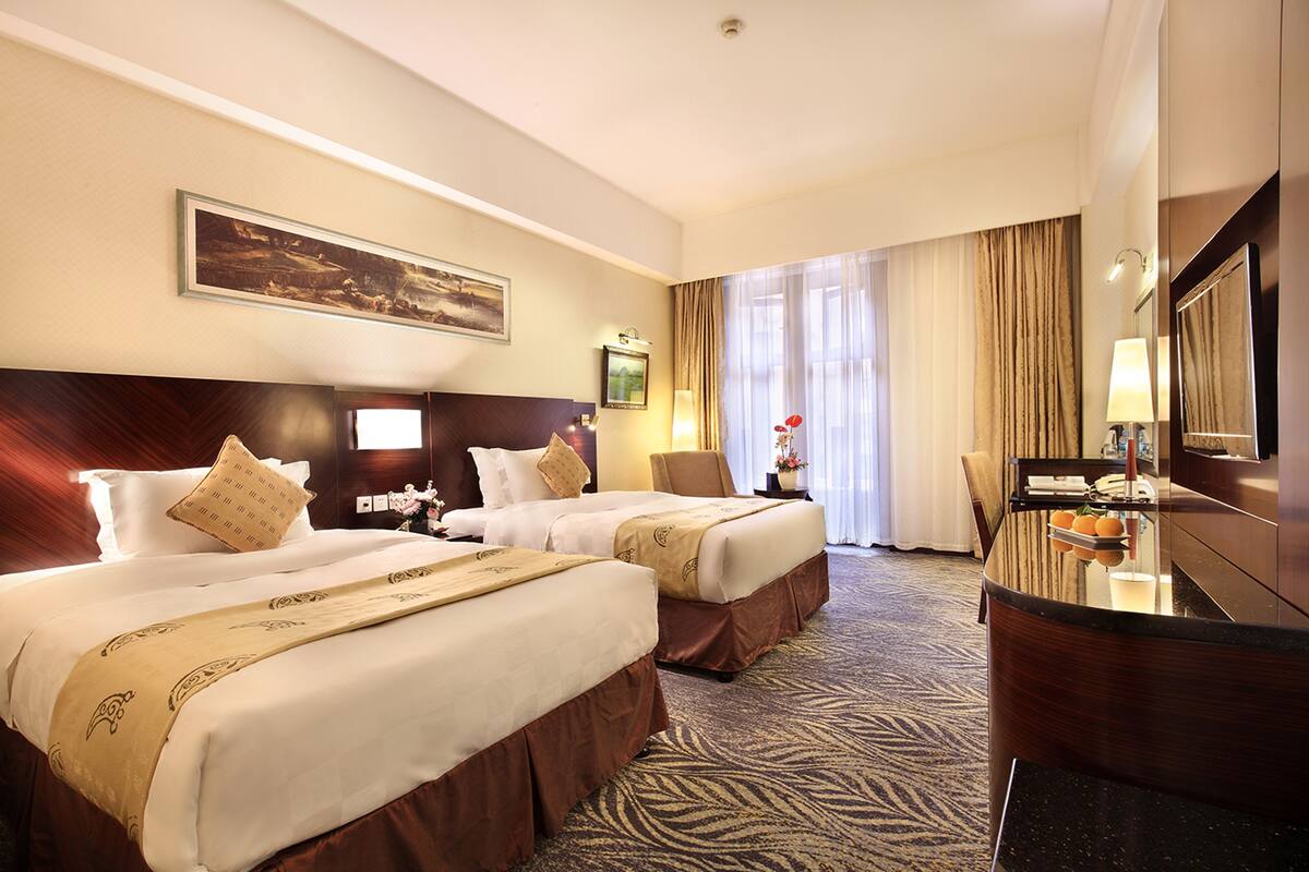 Quarto de hotel com duas camas, uma escrivaninha e uma janela grande com cortinas.