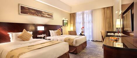 A hotel room with two beds, a desk, and a large window with curtains.