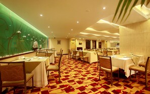 A hotel dining area with multiple tables and chairs, a patterned carpet, and a green decorative wall. - Guilin Lijiang Waterfall Hotel (Guilin)