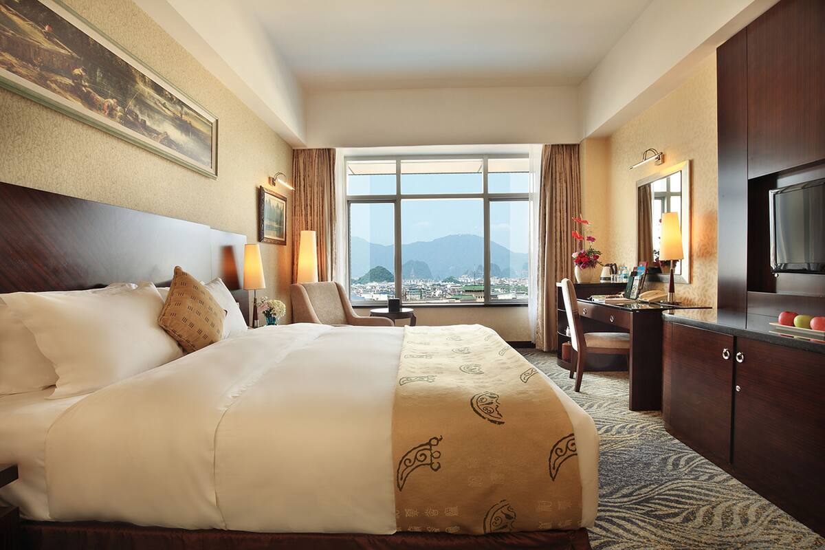 Quarto de hotel com uma cama grande, uma escrivaninha, uma cadeira, uma televisão e uma janela com vista para a cidade.