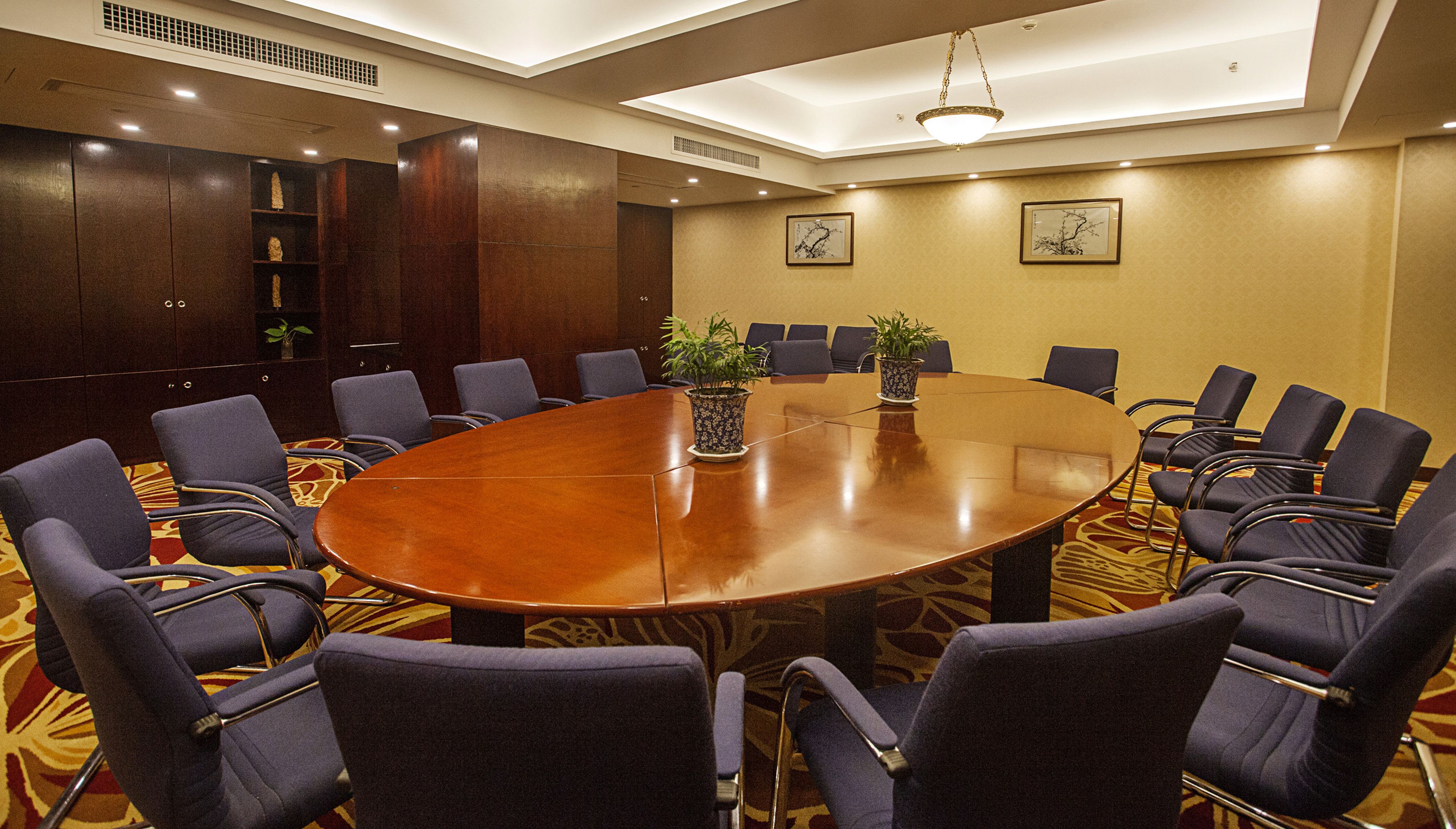Un salón de conferencias con una gran mesa ovalada, sillas tapizadas en azul y dos plantas en macetas.