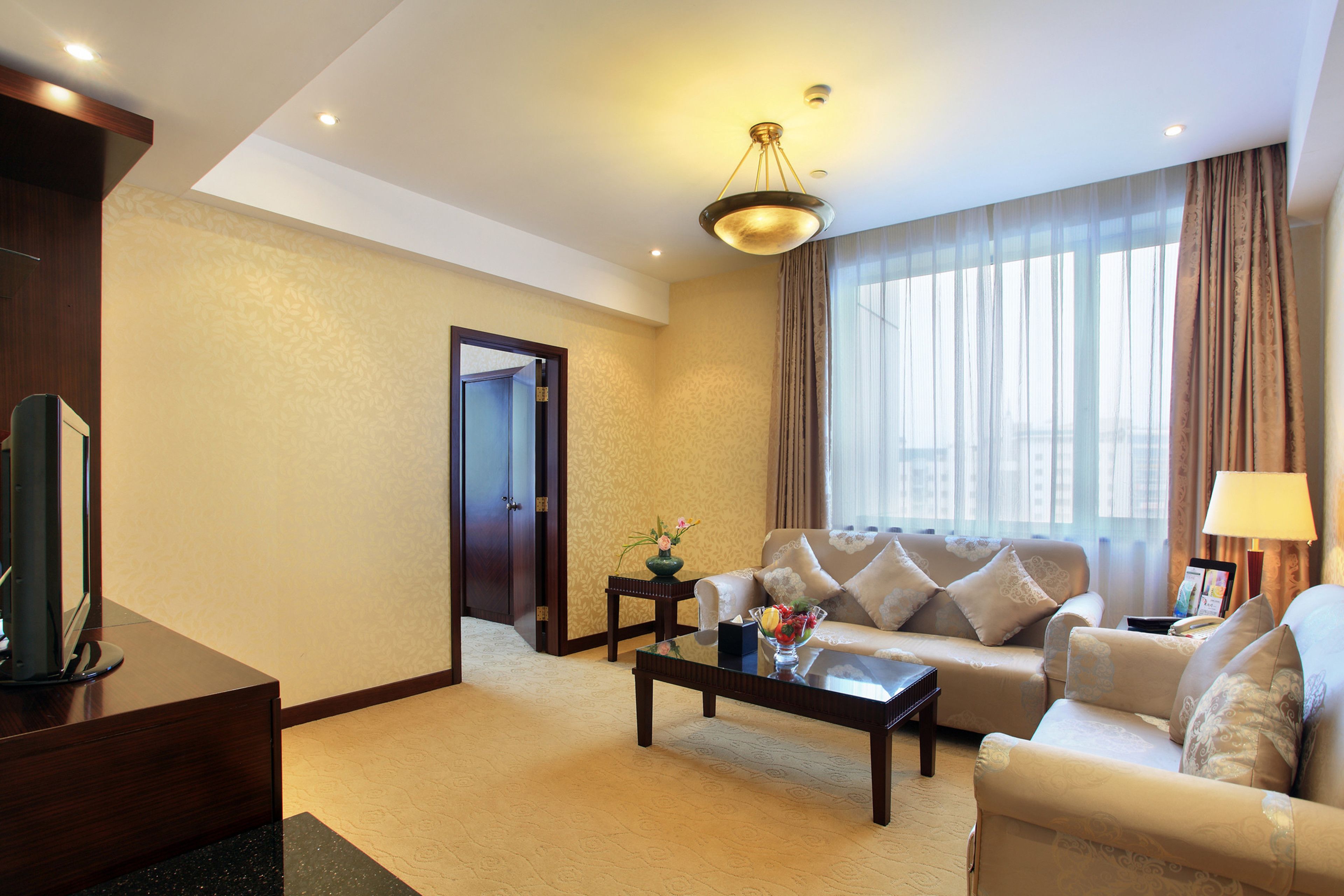 Quarto de hotel moderno com sofá, mesa de centro e televisão em um suporte.