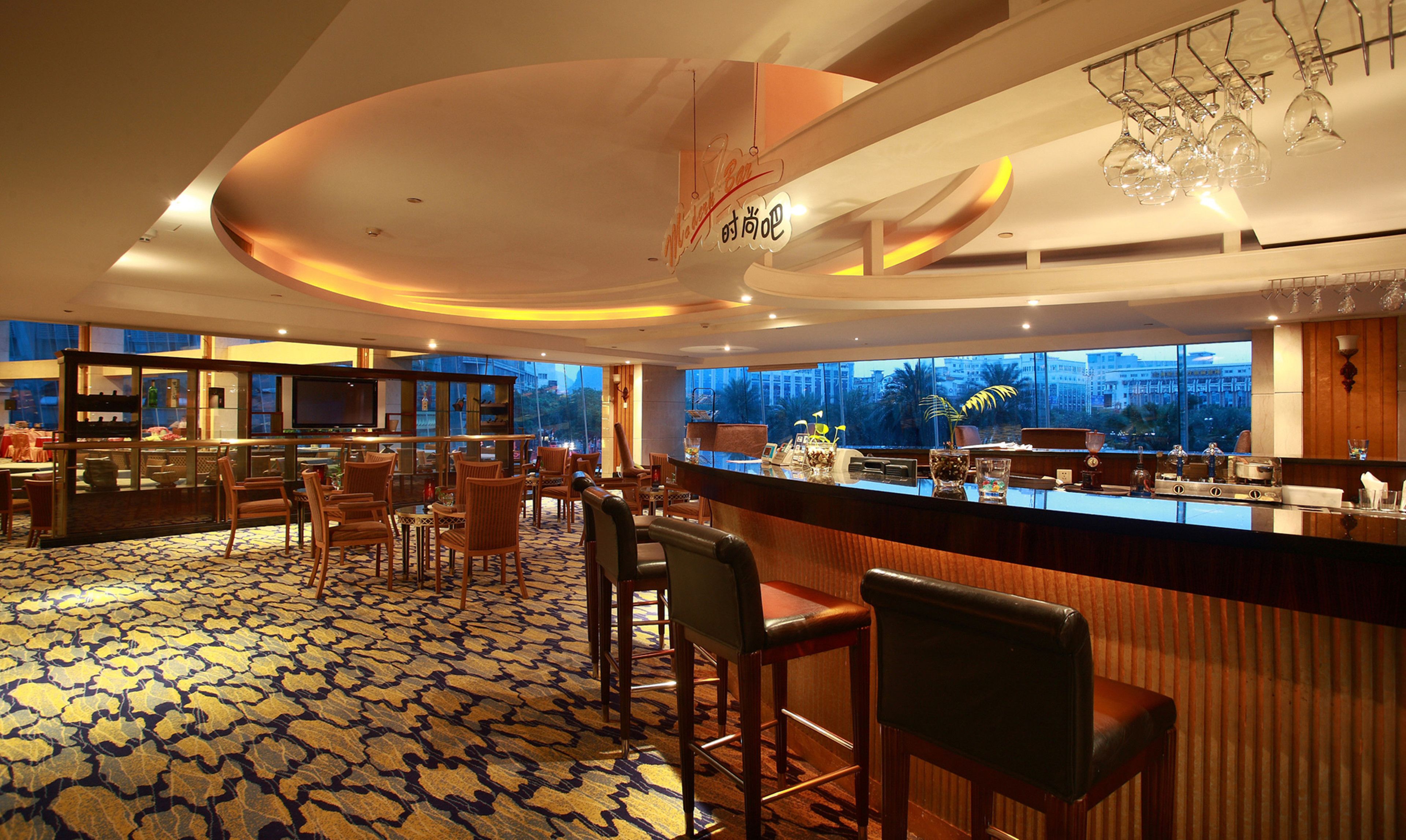 Un vestíbulo de hotel con zona de bar, asientos y un amplio ventanal con vistas a la ciudad.