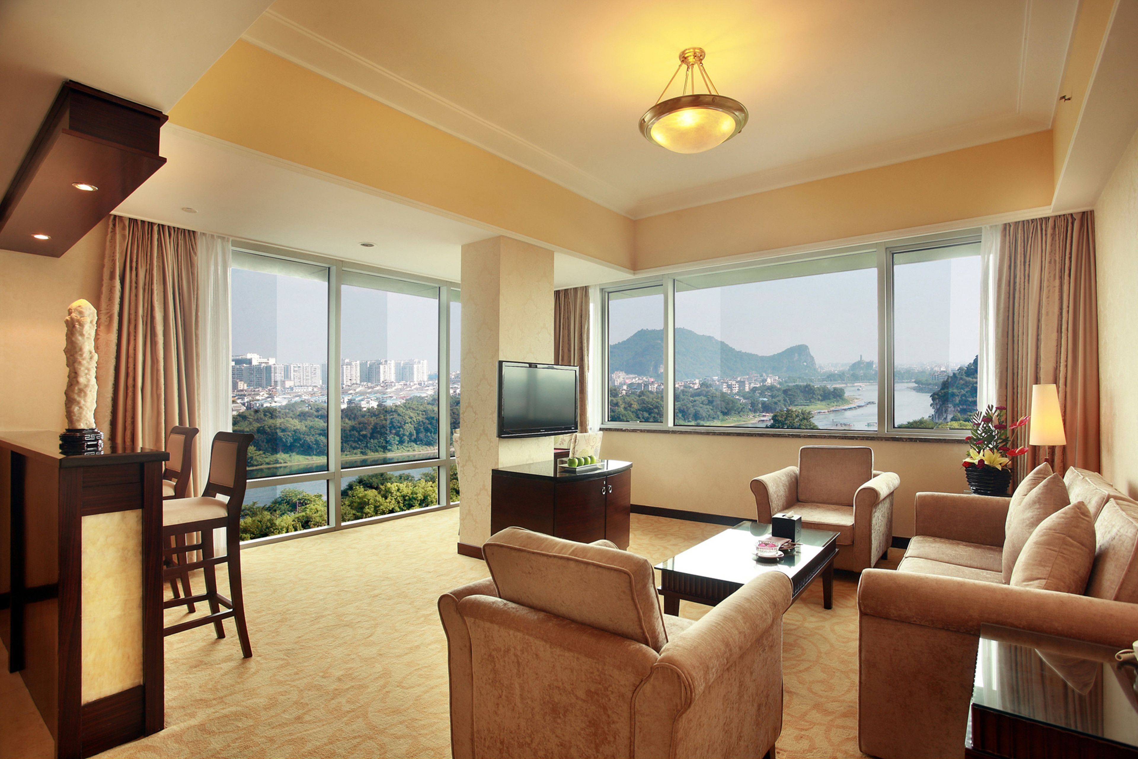 A spacious hotel room with a large window offering a city view, a flat-screen TV, and comfortable seating.