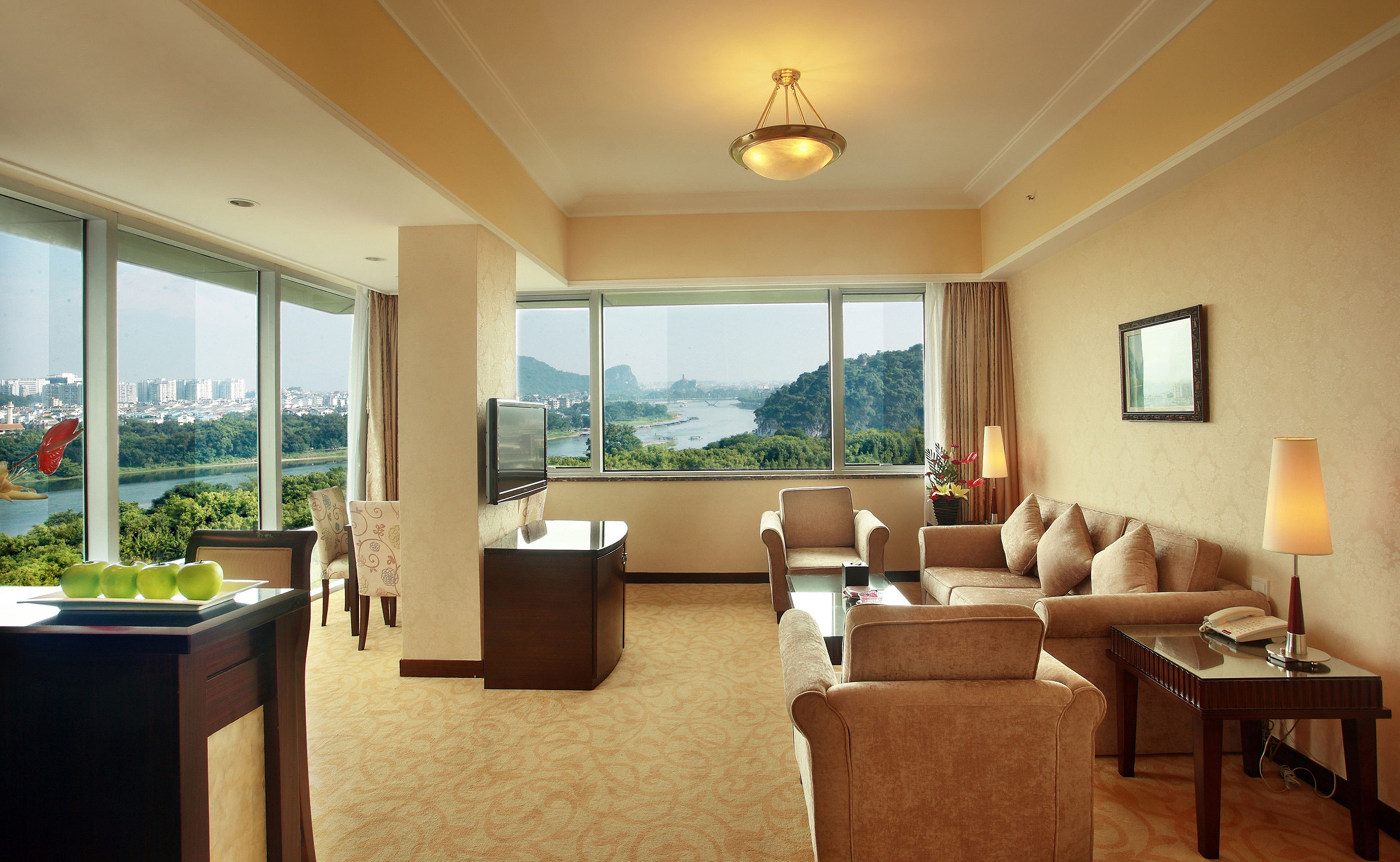 Ein Hotelzimmer mit großem Fenster und Blick auf Stadt und Fluss, inklusive Sofa, Schreibtisch und Fernseher.