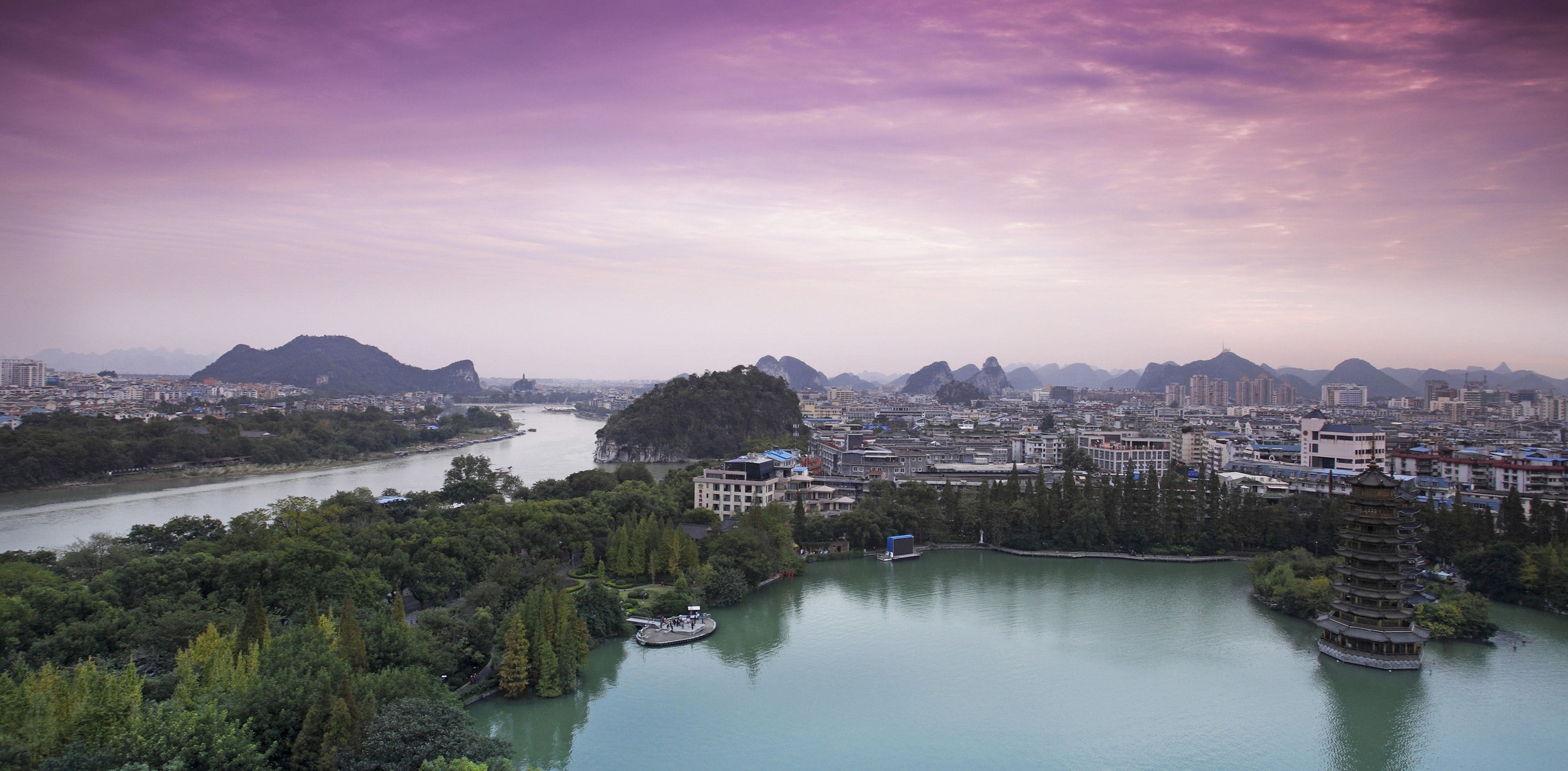 A cityscape with a river, a pagoda, and mountains in the background.