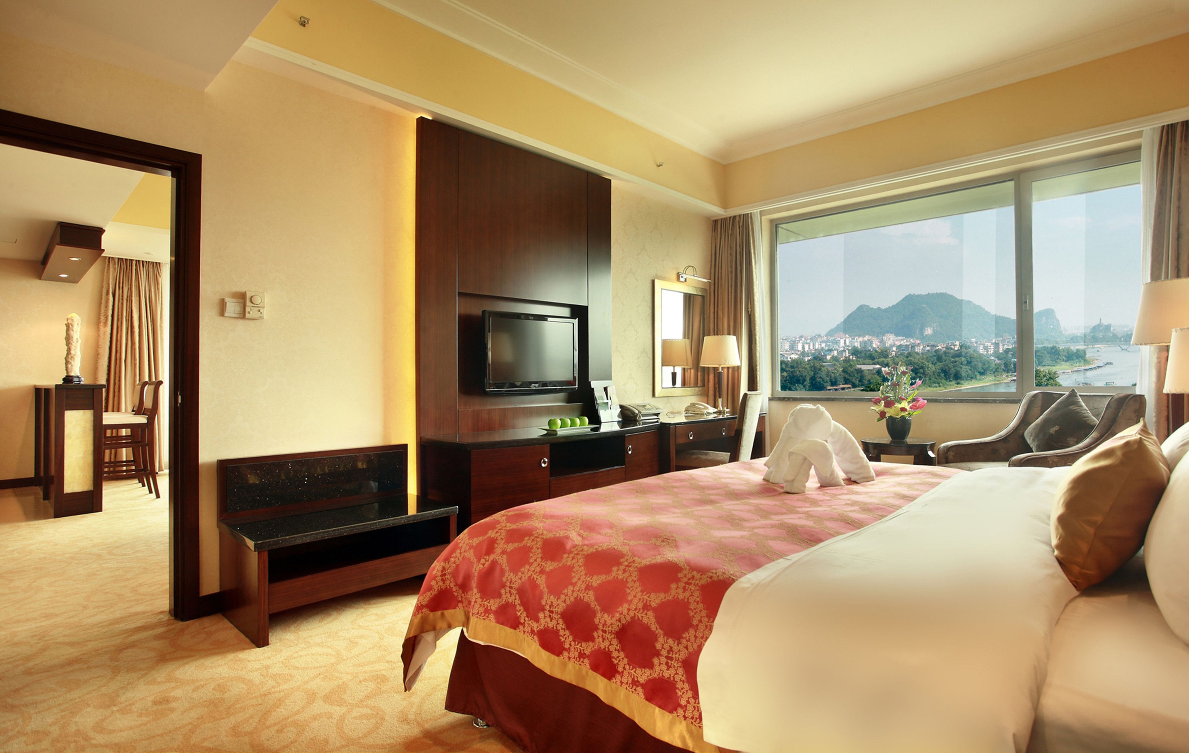 Habitación de hotel con una cama grande, televisión, escritorio y vista a un paisaje urbano.