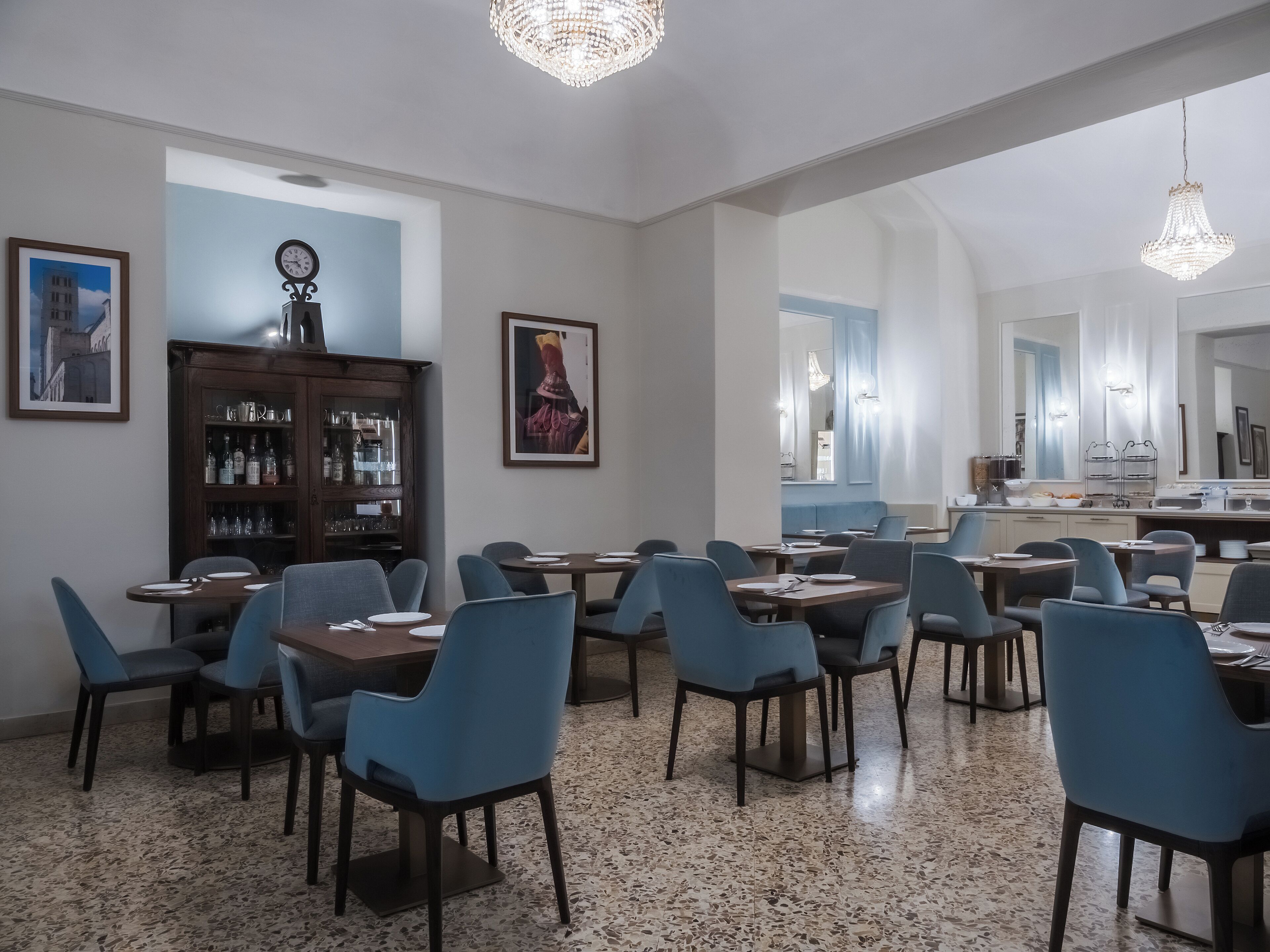 Zona pranzo con diversi tavoli e sedie, un armadietto in legno con bicchieri e un grande specchio.