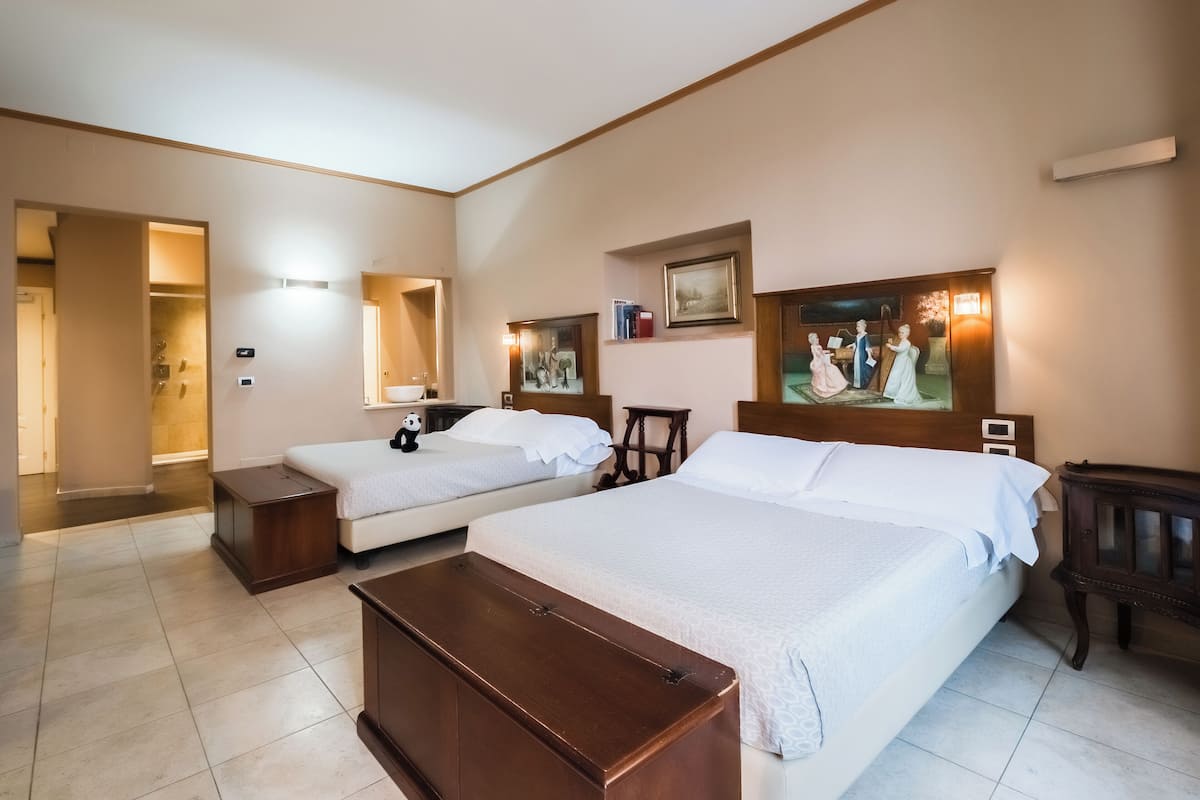 Habitación de hotel con dos camas, un banco de madera, un cuadro, una mesita y zona de ducha.